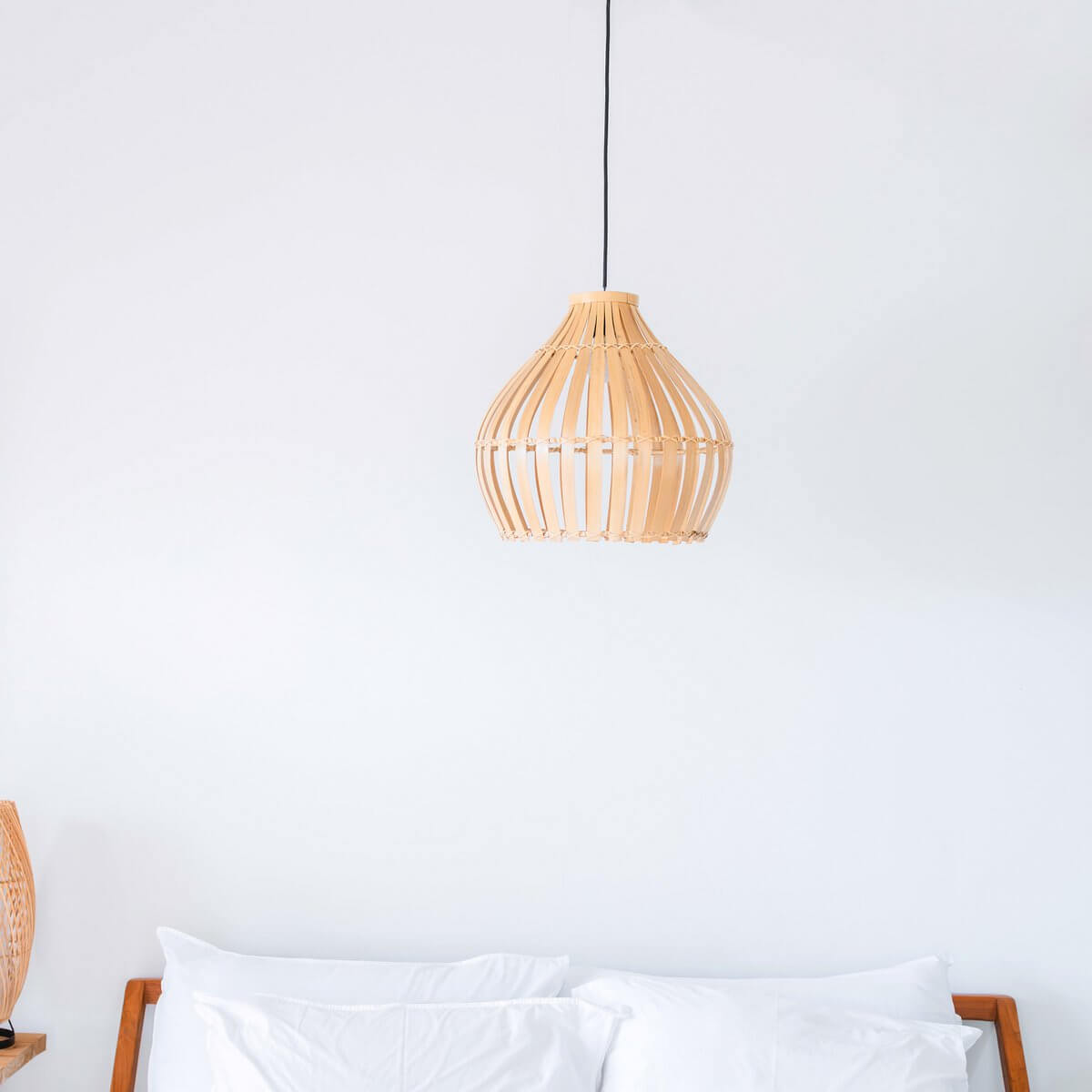 Bamboe lampenkap Kirma hangend boven een bed, elegant design met natuurlijke uitstraling, creërt gezellige sfeer in huis.