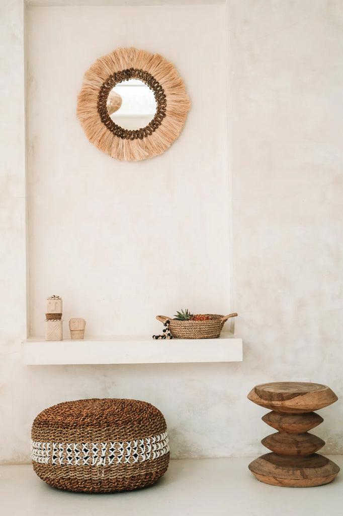 Stijlvol boho interieur met een handgemaakte rieten spiegel, houten kruk en decoratief mandje voor een warme sfeer in huis.