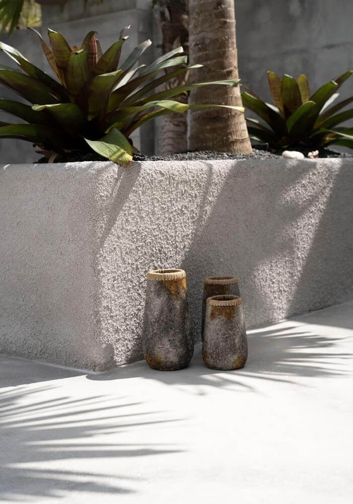 Handgemaakte boho vaas antiek grijs met raffia detail, buiten in een zonnige tuin met tropische planten