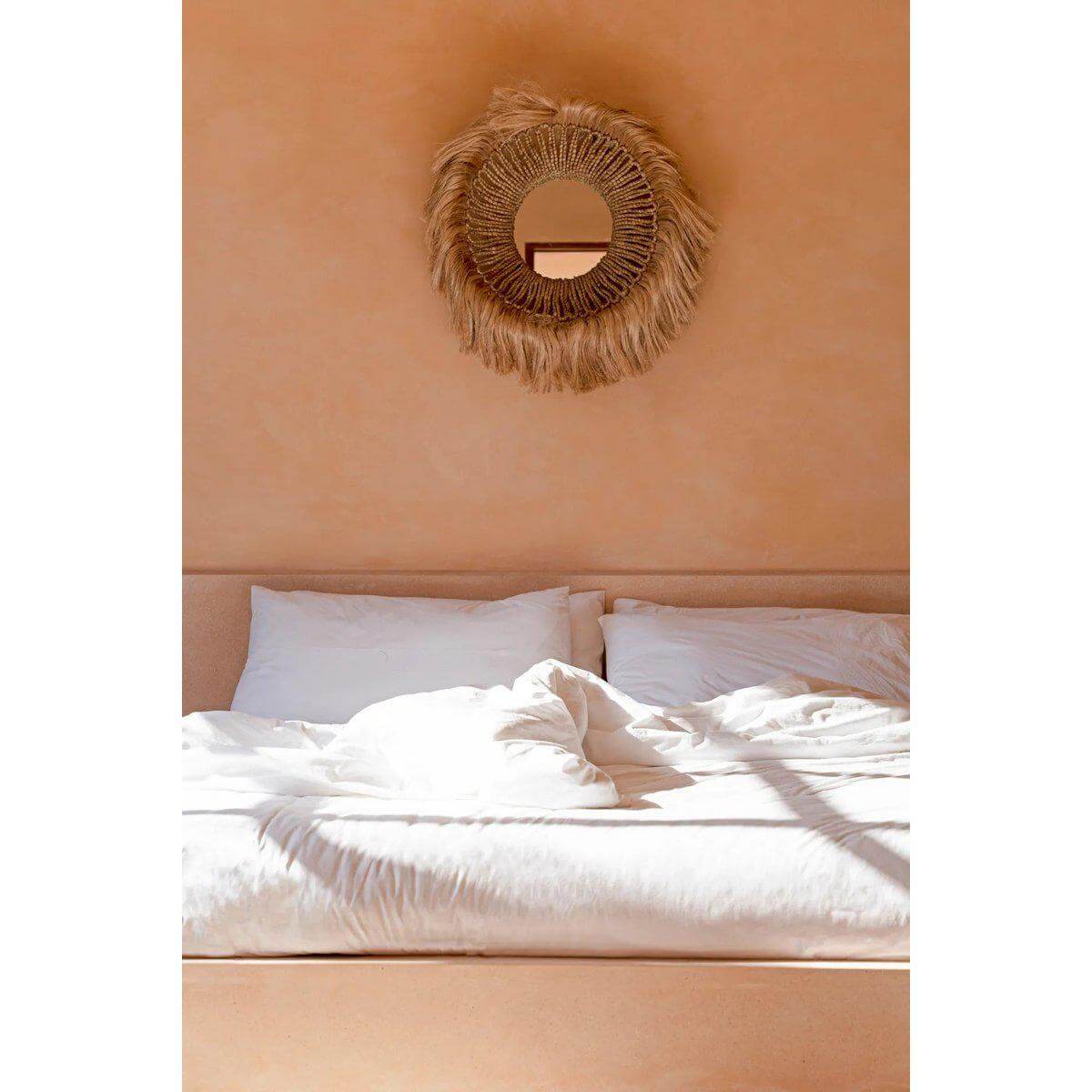 Elegante Abaca spiegel boven bed, handgemaakt van duurzaam gras, voegt natuurlijke stijl en diepte toe aan interieur.