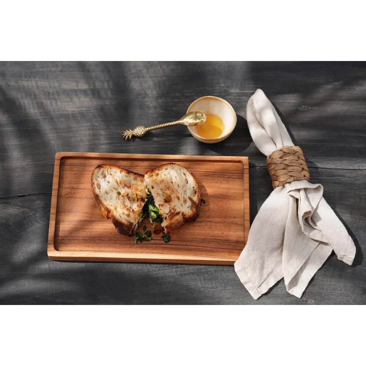 Bohemian dining scene with De Ananas Theelepel in gold, featuring rustic sandwich on wooden board and elegant table setting.