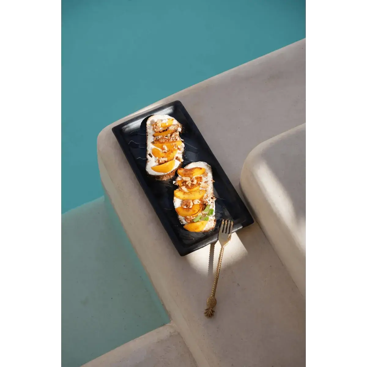 Bohemian gold pineapple fork on elegant stone slab by pool, paired with gourmet appetizers, showcasing tropical luxury dining.
