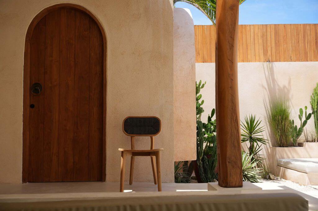 Teakhouten Arigato eetkamerstoel buiten bij houten deur en planten