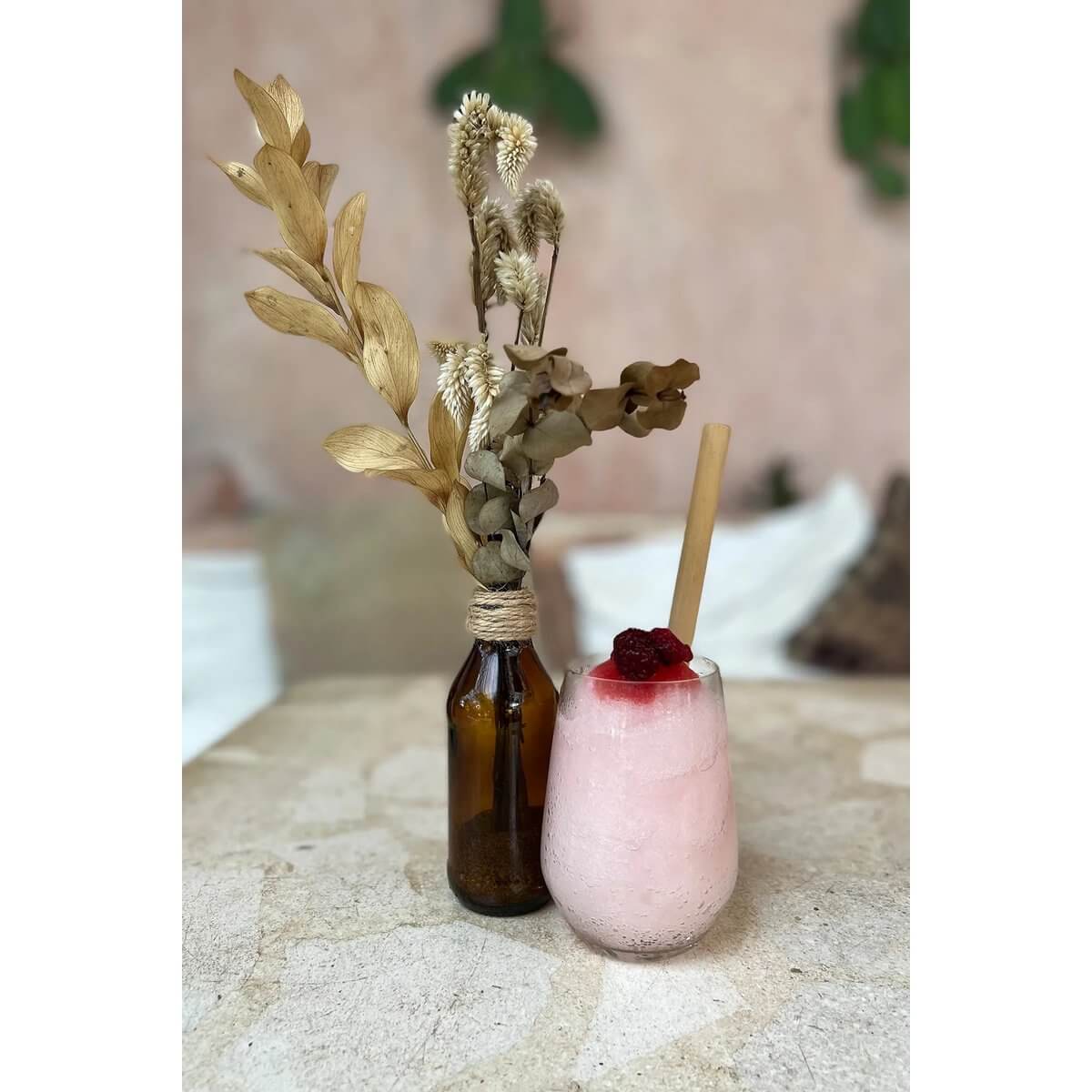 Bohemian smoothie set with bamboo straw and dried floral arrangement on stone table, showcasing eco-friendly dining vibes.