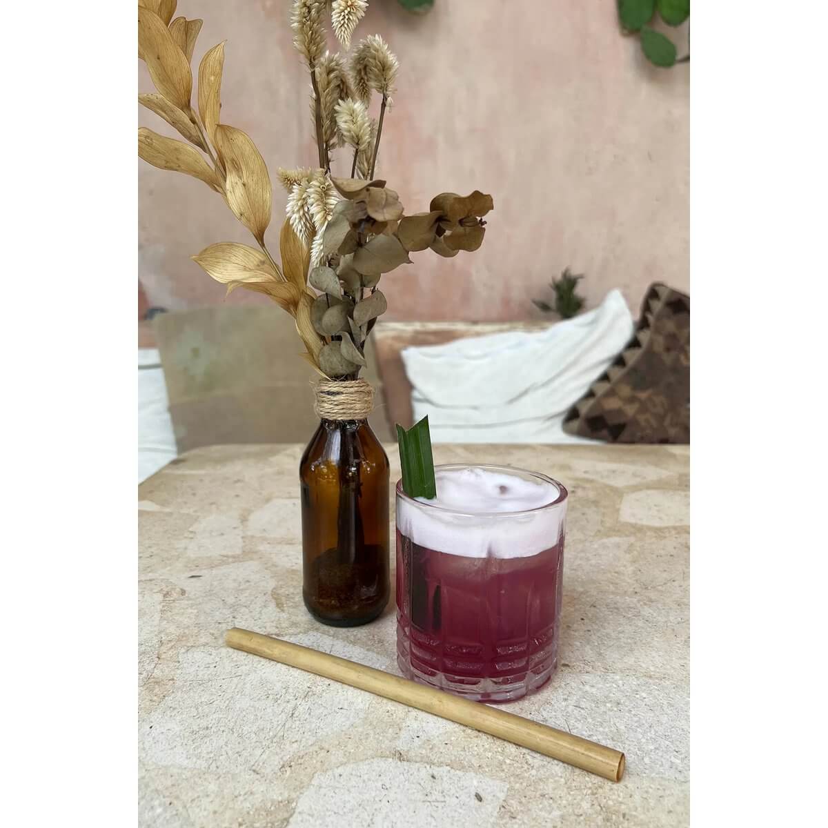 Bohemian style drink with reusable bamboo straw next to dried flowers on a rustic table.