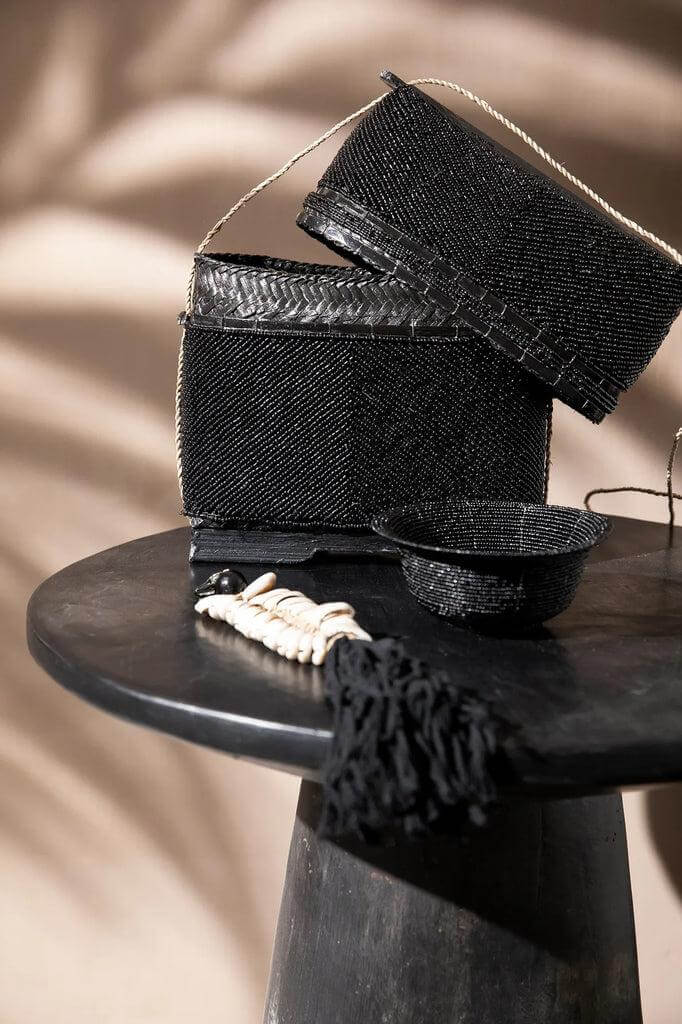 Zwarte De Beaded Schatkist van bamboe, kralen en zeegras, ideaal voor stijlvolle opbergruimte op een elegant zwart oppervlak.