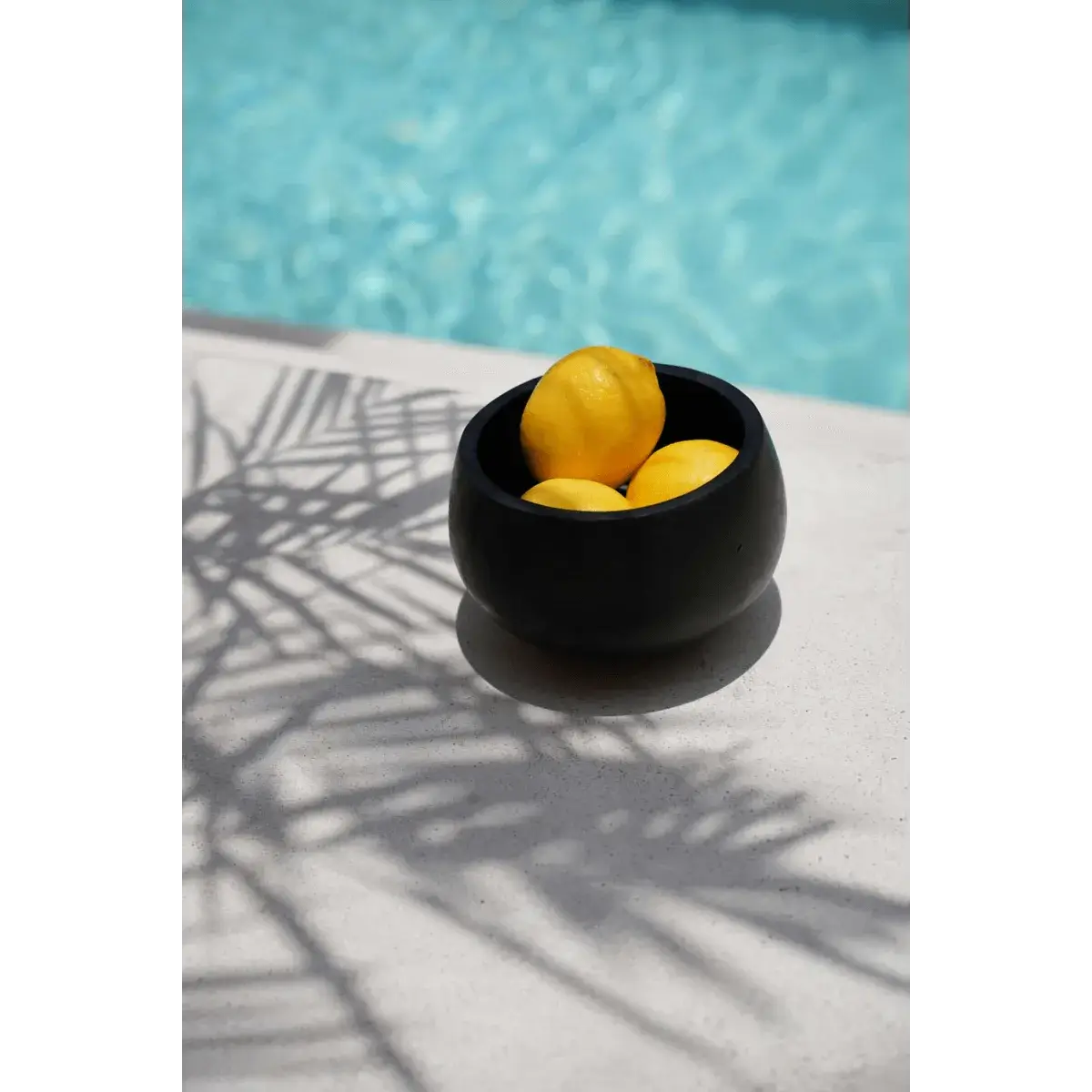 Bohemian De Bondi Black Bowl with lemons by a pool, showcasing a multifunctional and stylish teak wood design.