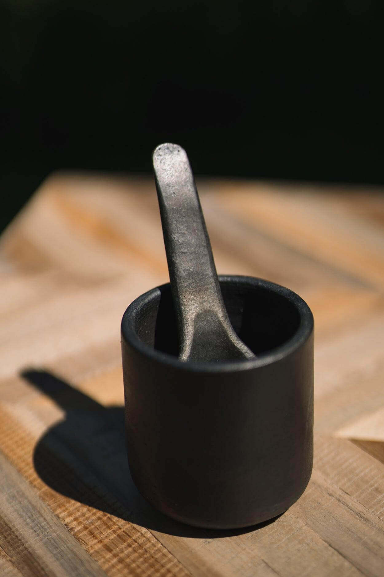 Stijlvolle zwarte beker uit de Burned collectie op houten tafel, perfect voor voedselstyling en veelzijdig gebruik in de keuken.
