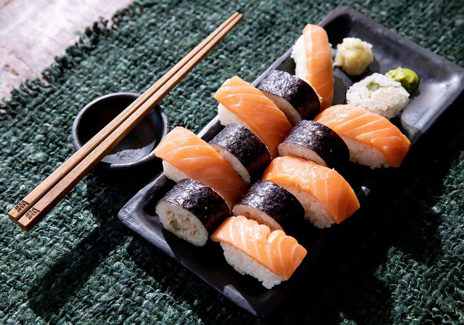Sushi op zwarte schaal met wasabi en gember, geserveerd op een groene placemat, vergezeld door houten eetstokjes.