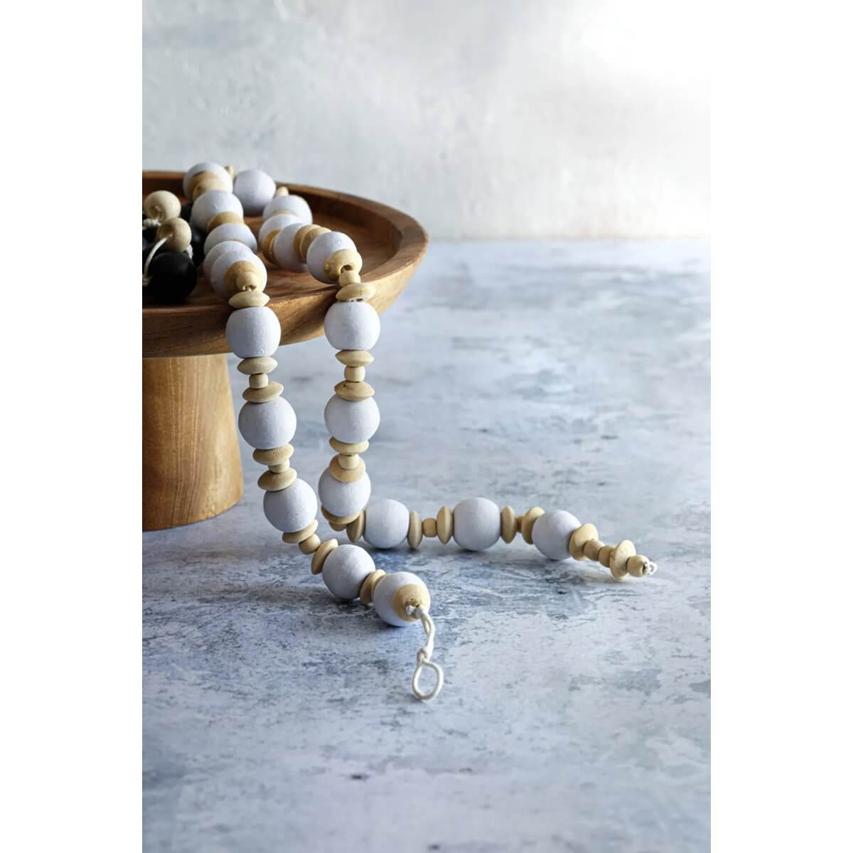 Bohemian De Canggu ketting in natuurlijk wit met houten kralen, elegante rondingen en strakke lijnen, ligt op een houten schaal.