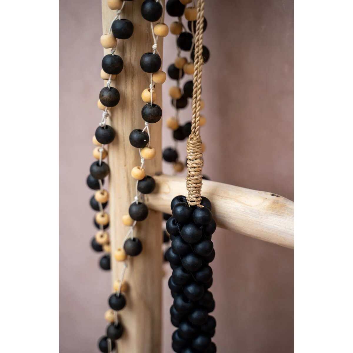 Bohemian-style De Canggu ketting with natural black and beige wooden beads elegantly draped over a ladder, showcasing timeless charm.