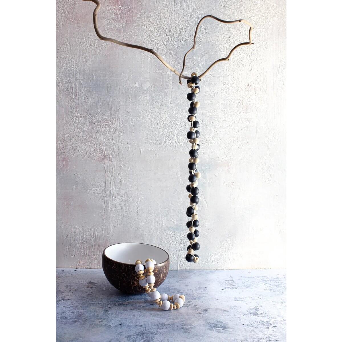 Bohemian Canggu ketting with natural black beads, hanging from a branch with stylish curves, next to an elegant coconut bowl.