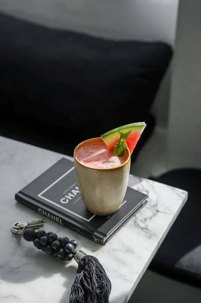 Houten beker met vruchtencocktail op boek, versierd met watermeloen en munt, op marmeren tafelblad.