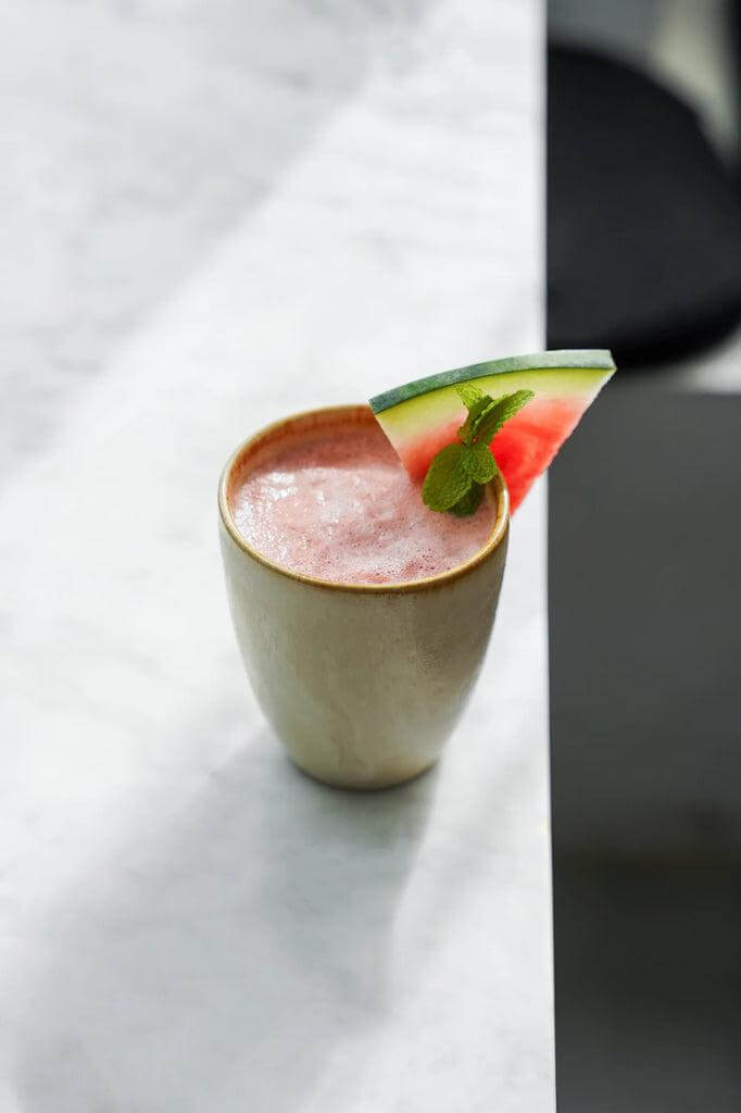 Verfrissende smoothie geserveerd in een keramische beker met watermeloen en munt garneersel op marmeren tafel.