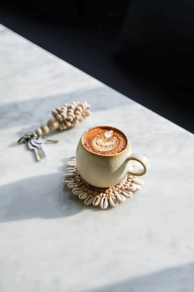 Elegante witte koffiemok op marmeren tafel, versierd met schelpenslinger, perfect voor brunch of ontbijt.