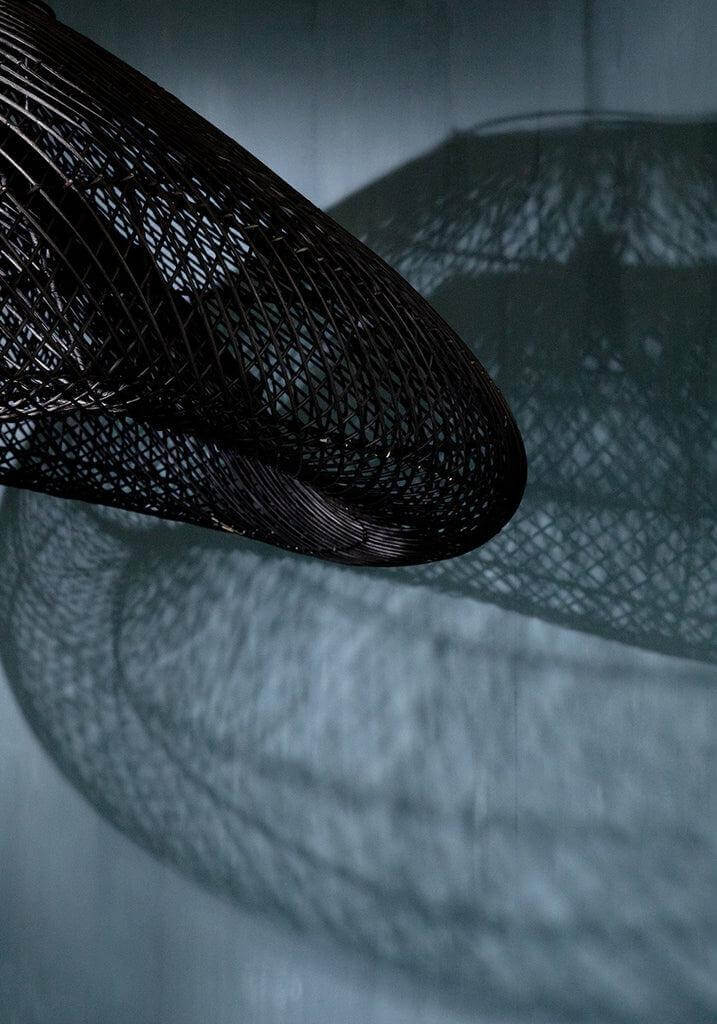Close-up van de XXL De Cloud Hanglamp in zwart rotan, met prachtige schaduwen op de muur. Ideaal voor een bohemian interieur.