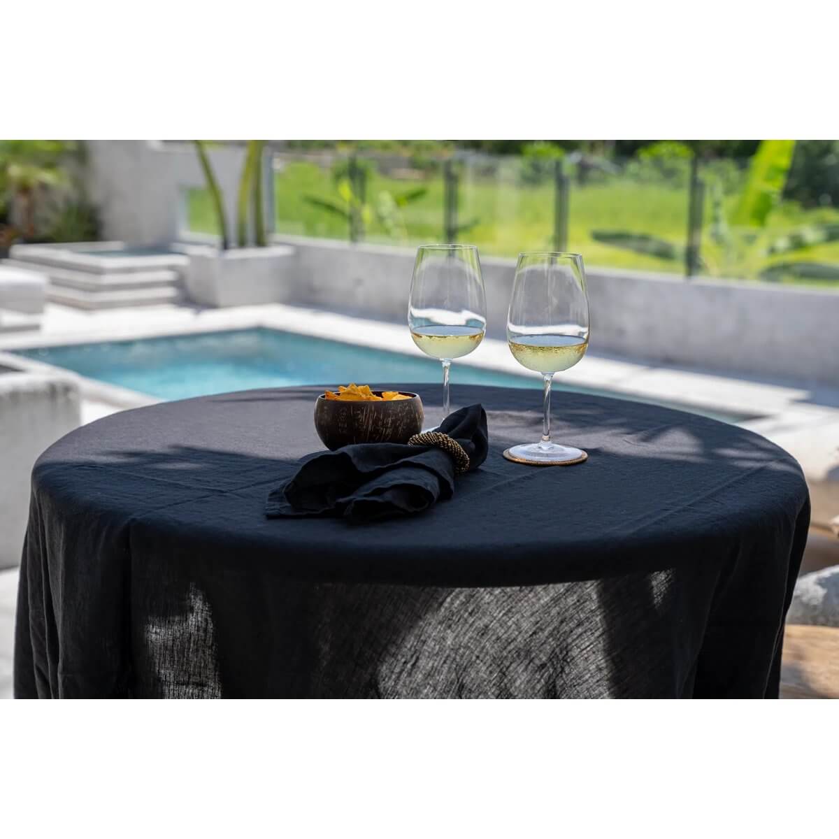Bohemian-style poolside setup with De Coco coconut bowls and wine glasses on a black tablecloth.
