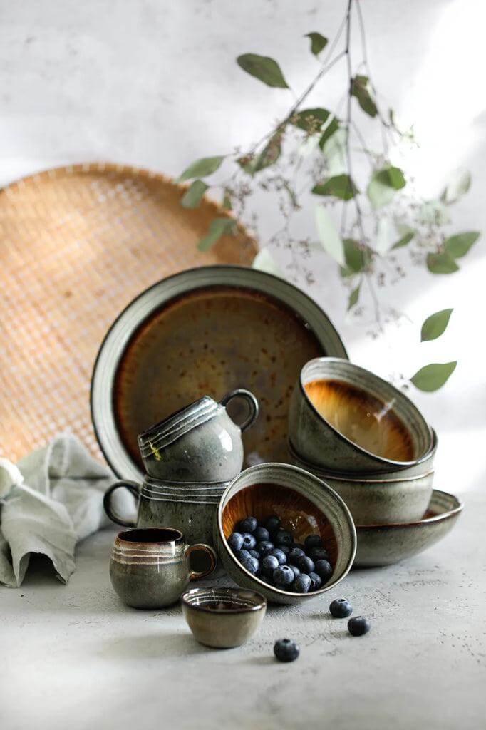 Charmant servies van Portugese aardewerk met mokken en borden, ideaal voor brunch of diner, vaas met takjes als achtergrond.