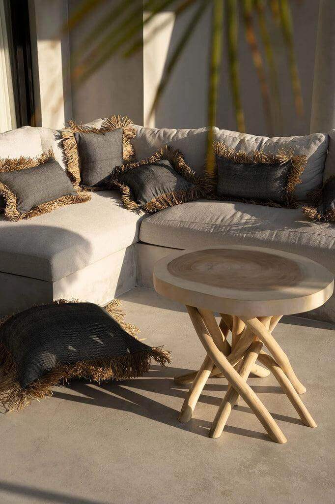 Stijlvol interieur met zwarte en natuurlijke kussenhoezen met raffia franjes op een loungebank, zomerse vakantie sfeer.