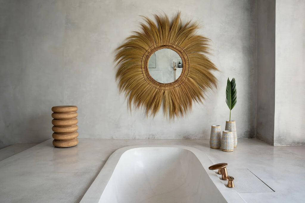 Stijlvolle badkamer met moderne badkuip, rotan spiegel, en decoratieve vaas voor een serene sfeer.