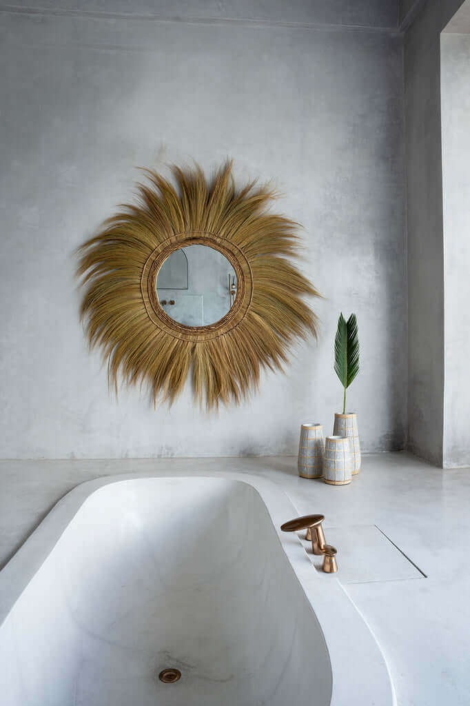 Moderne badkamer met bad, grote ronde spiegel met rotan details en stijlvolle vazen op de achtergrond.