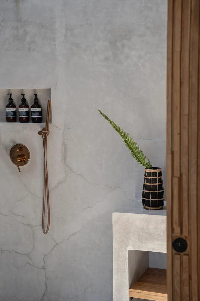 Zwarte terracotta vaas met rotan detail op badkamerplank naast douche, stylish kustgevoel met gedroogde varen. Niet waterdicht.