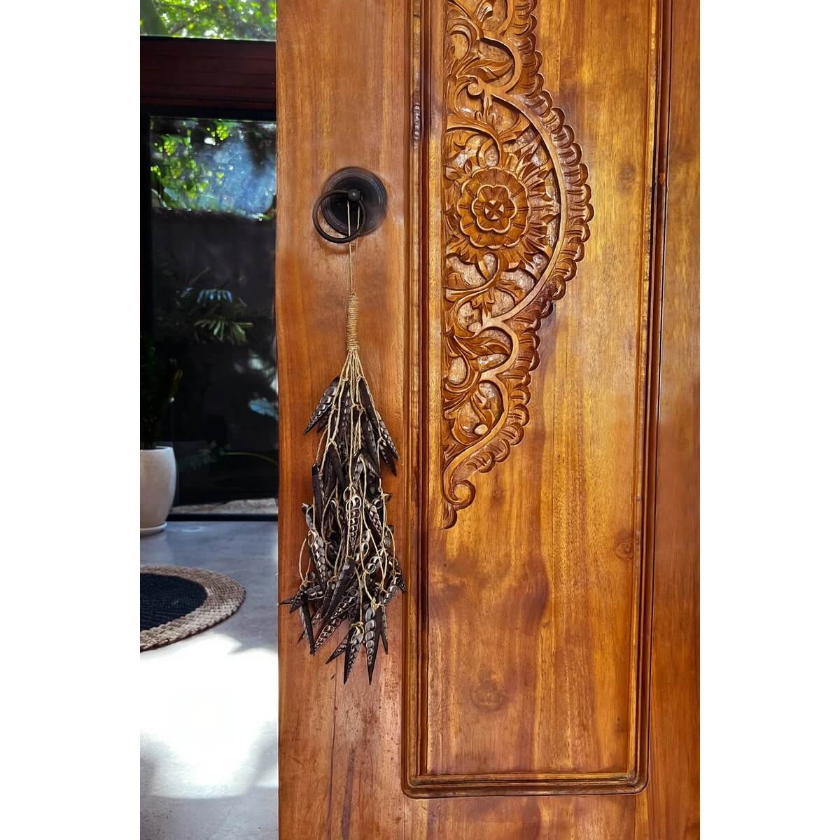 Bohemian brown shell tassel with unicorn horn design hanging on carved wooden door, adding unique decorative charm.
