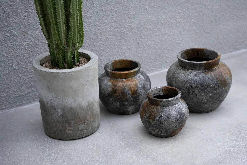 Drie terracotta vazen in antiek grijs met zilverachtige glans naast een cactus in een betonnen pot.