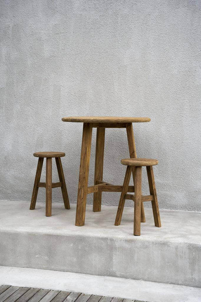 Twee Fusuma barkrukken van teakhout naast een bijpassende outdoor tafel op een terras. Stijlvolle en duurzame meubelset voor buiten.