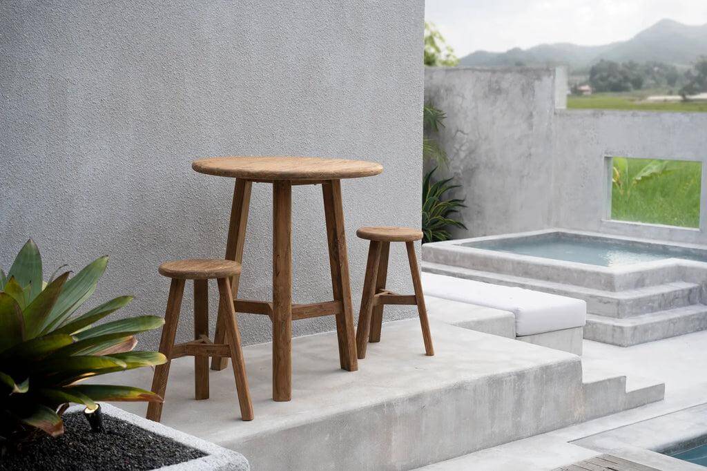 De Fusuma Bartafel van hergebruikt teakhout op een moderne patio met uitzicht op een serene groene achtergrond.