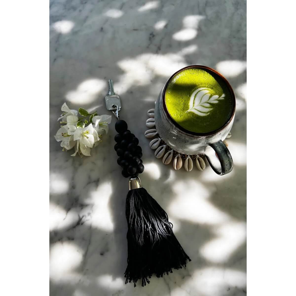 Bohemian black wooden bead keychain with tassel, beside a flower and a matcha latte on a marble surface, exuding refined elegance.
