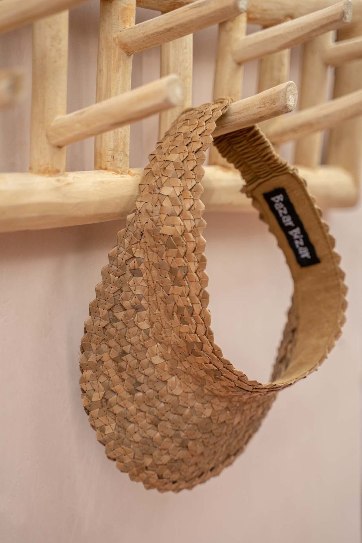 Handgemaakt teakhouten kapstok met natuurlijke uitstraling en opgehangen rieten mandje in interieur. Praktisch en decoratief design.