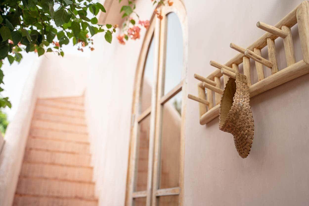 Natuurlijk massief teak kapstok aan muur met hoed nabij boogvormig raam, decoratief en praktisch voor hal of badkamer.