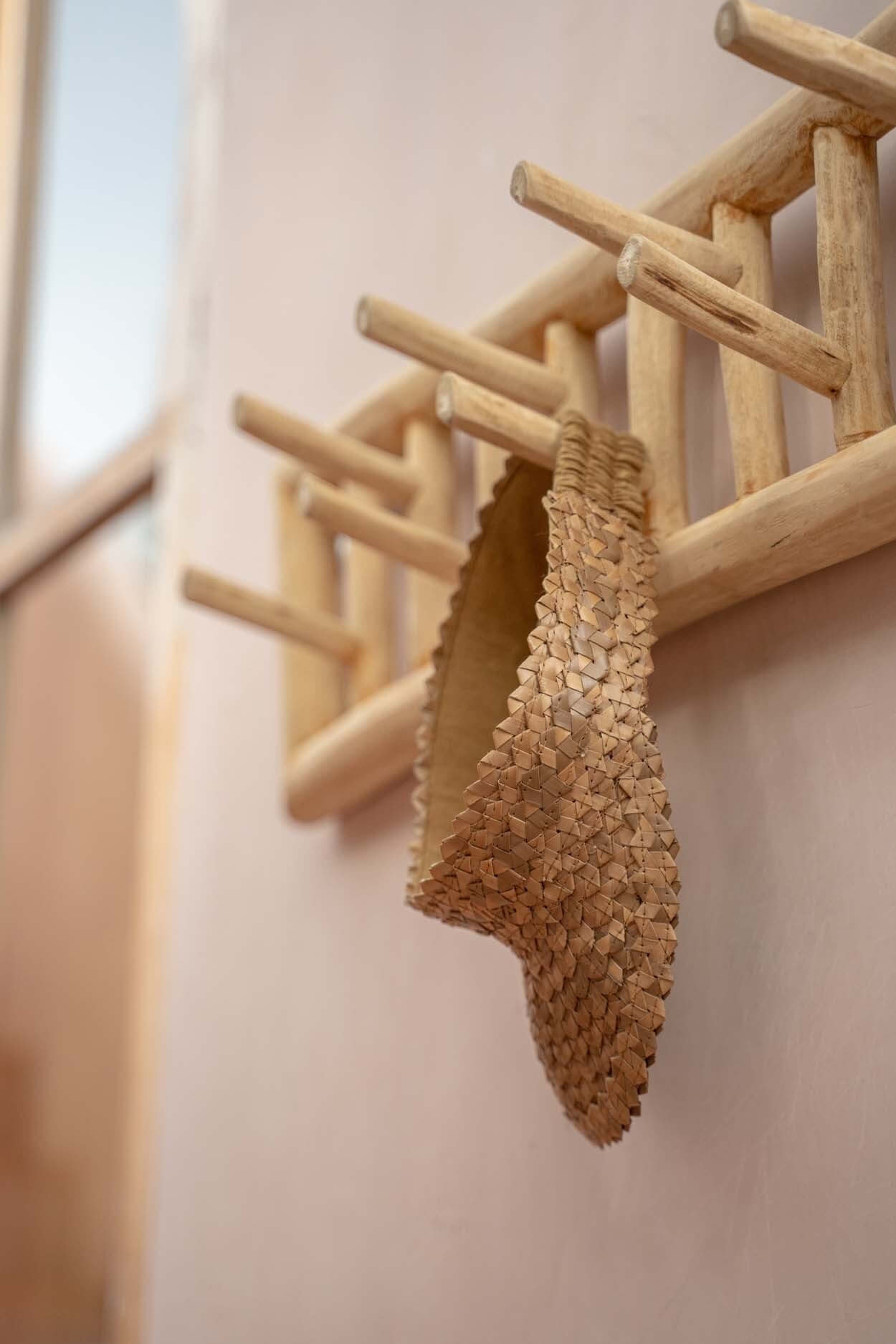 Massief teakhouten kapstok met decoratieve mand hangt in een sfeervolle kamer.