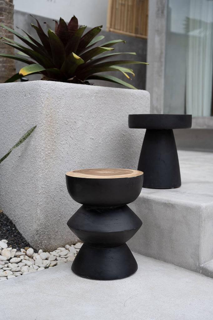 Twee zwarte Karbun krukken van suarhout op een betonnen terras, perfect voor gebruik binnenshuis als bijzettafeltje of krukje.