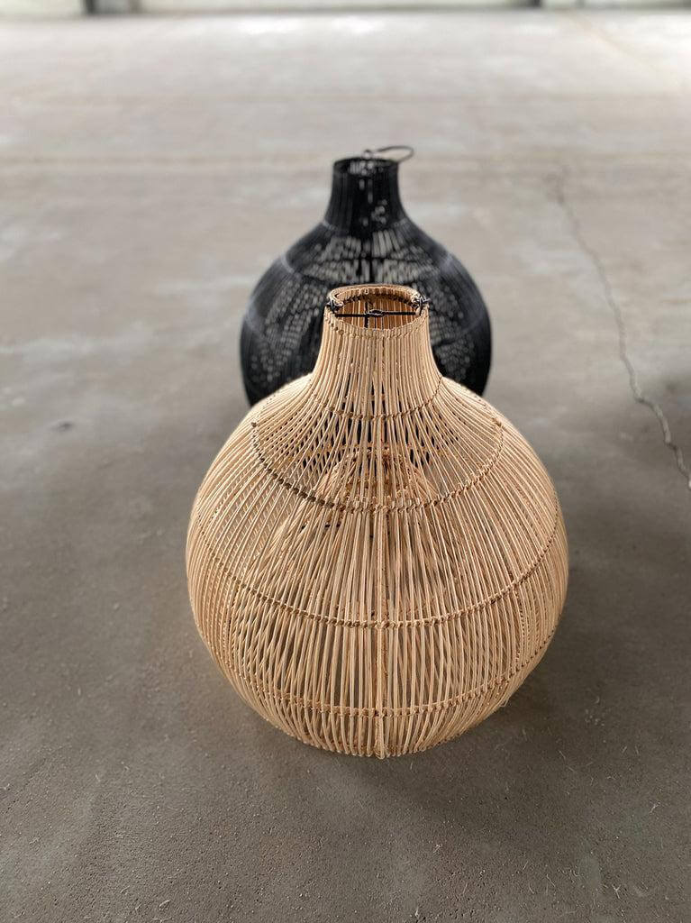 Ronde rotan hanglampen in natuurlijke en zwarte kleur op een betonnen vloer.