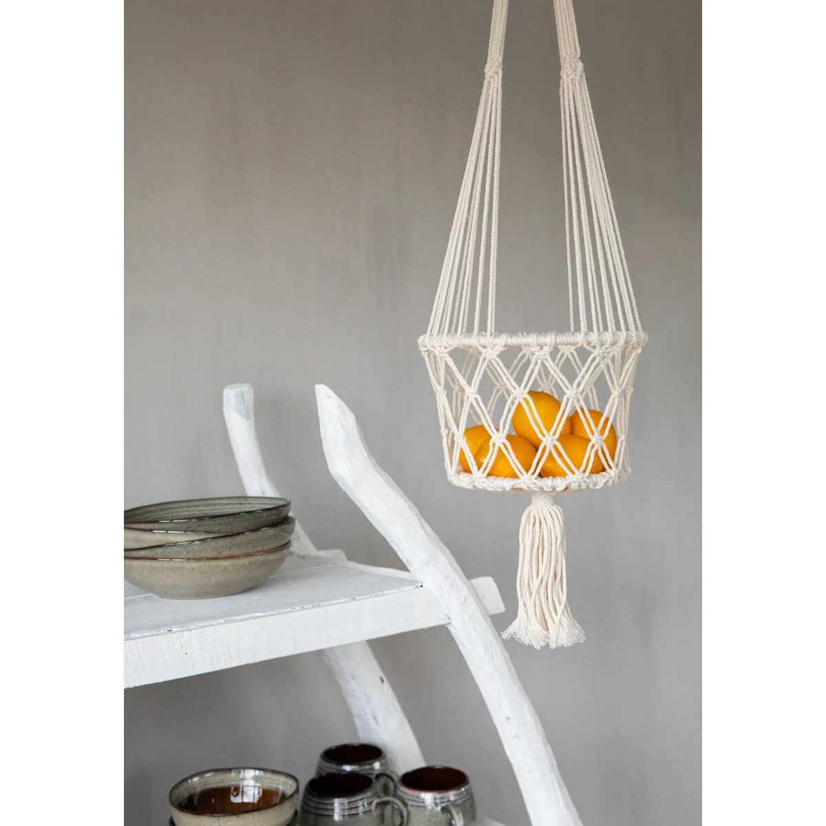 Bohemian style macramé plant hanger in white, holding vibrant oranges, adding decorative charm to indoor spaces.