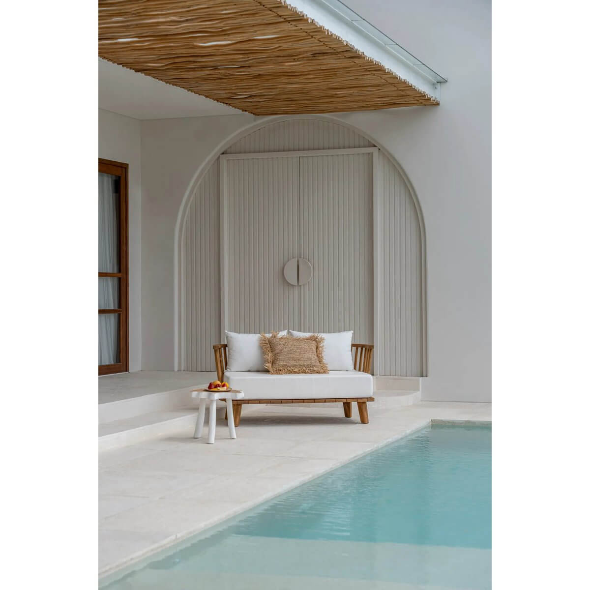 Bohemian outdoor two-seater sofa made from reclaimed teak with white cushions, elegantly placed by a serene pool.