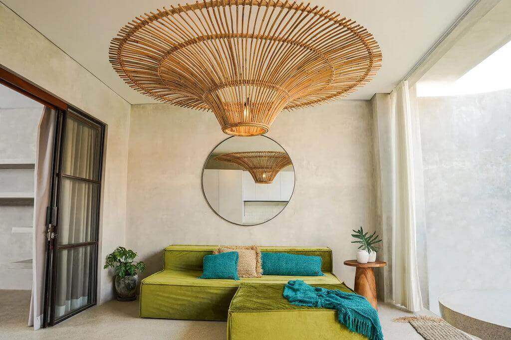 Stijlvolle woonkamer met groene bank en aqua kussenhoes, bohemian sfeer, grote rotan lamp en ronde spiegel, moderne inrichting.