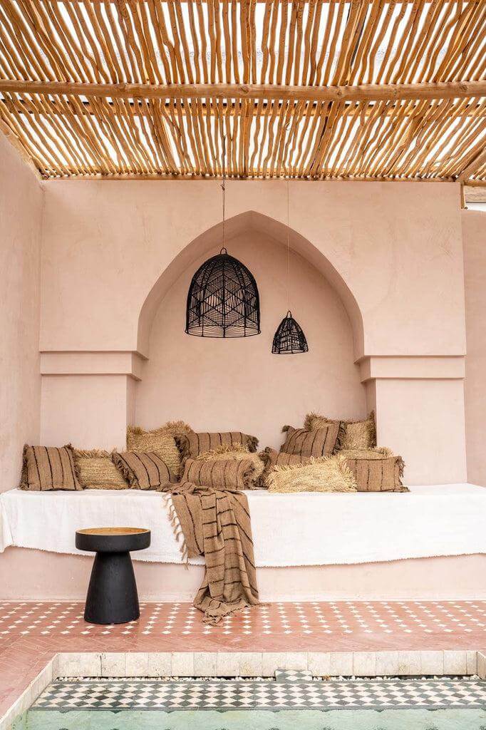 Stijlvolle boho zithoek met natuurlijke elementen, kussens en houten dak, perfect voor een serene, ontspannen sfeer in tuin of patio.