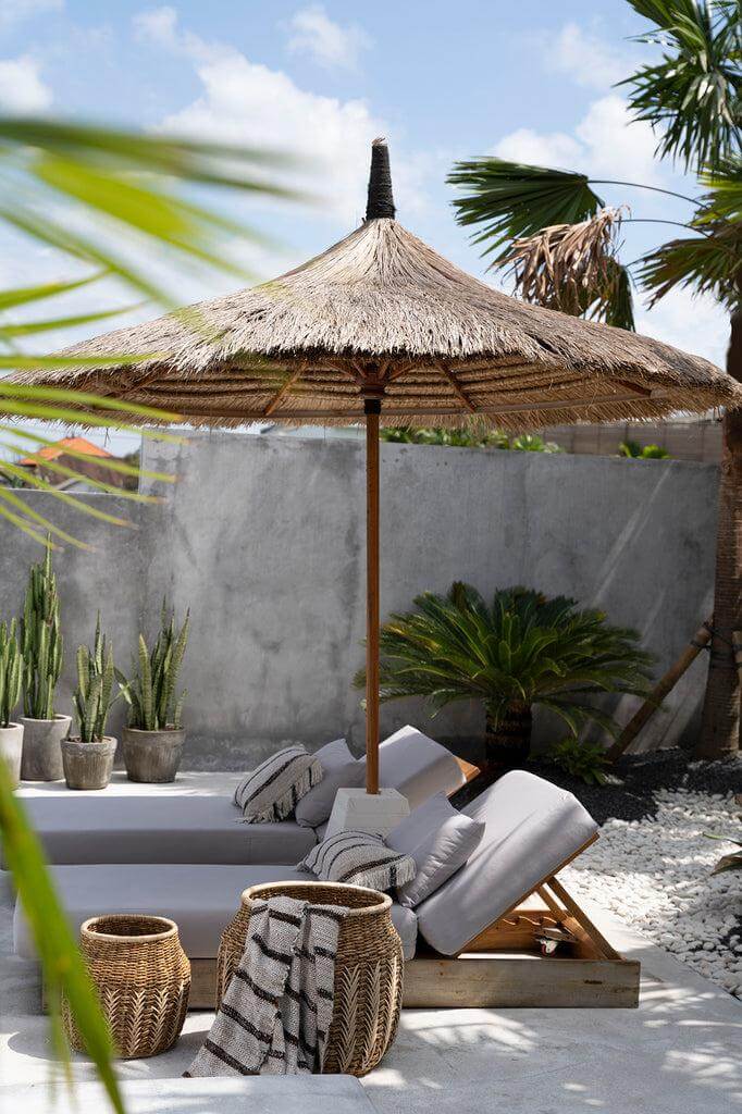 Tropisch terras met rieten parasol, chaise longues en decoratieve manden, perfect voor een boheemse sfeer in de tuin.