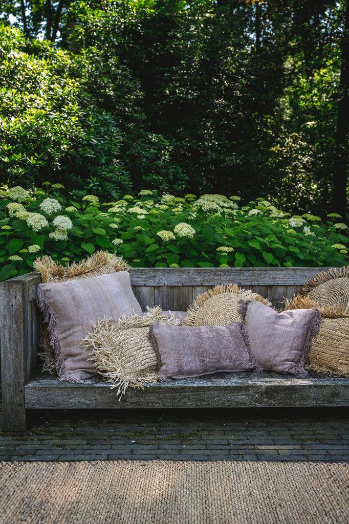 Houten bank met effen en franje kussens voor een boho vibe, omringd door groen in de tuin.