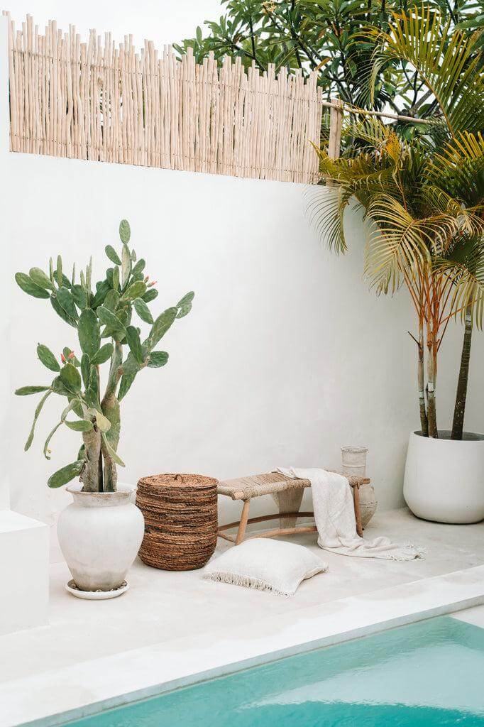 Een stijlvolle buitenruimte met een crème kussenhoes, een boho-touch en weelderige planten bij een zwembad, perfect voor ontspanning.
