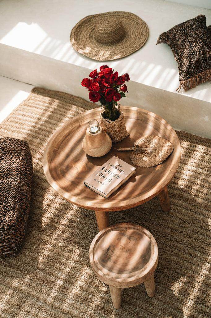 Gezellige boho zithoek met houten tafel, rode rozen en decoratieve kussens op een gevlochten vloerkleed in natuurlijke tinten.