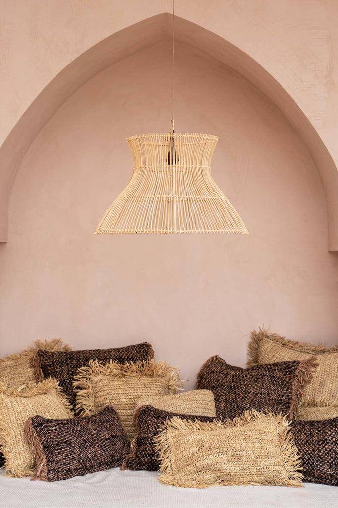 Gezellige zithoek met boho kussens en bamboe lampenkap in een gebogen nis tegen een beige muur.