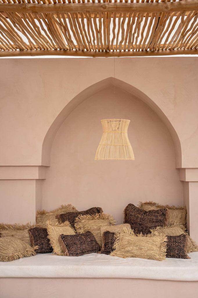 Rustieke zithoek met boho-kussens in zwart koper en beige, onder een houten afdak. Sfeervolle en chique inrichting voor binnen of buiten.
