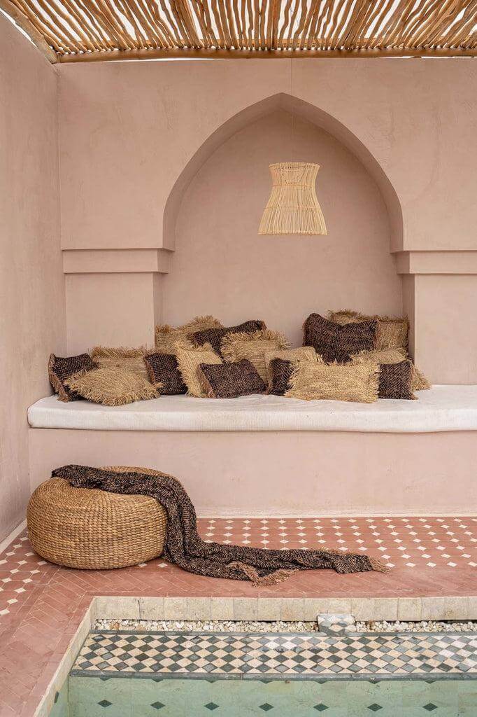Gezellige zithoek met boho kussens en een geweven poef bij een stijlvol zwembad. Perfect voor een serene tuinsfeer.