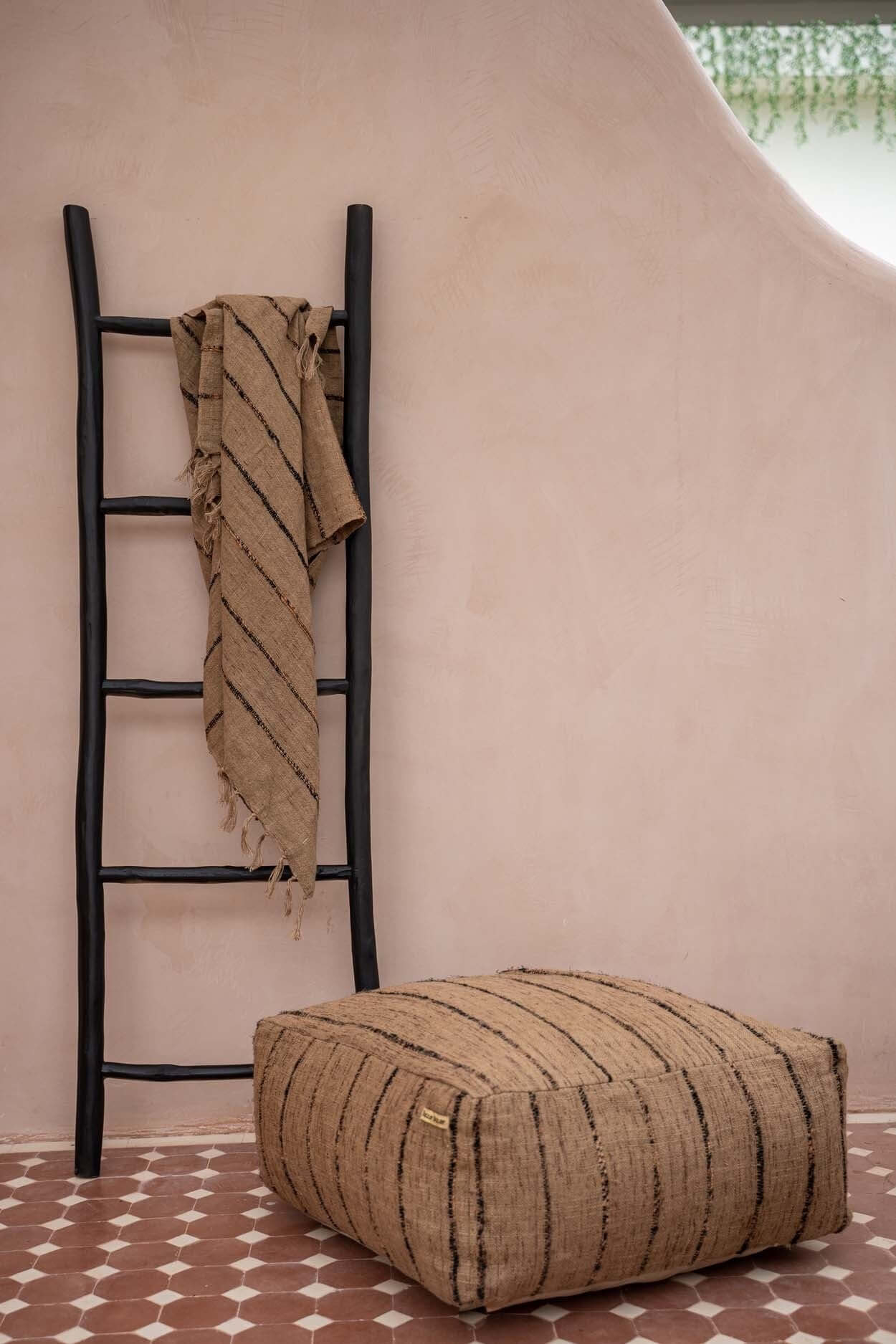 Beige en zwarte katoenen poef naast decoratieve ladder, perfect voor stijlvolle zitplek in woon- of binnenruimte.