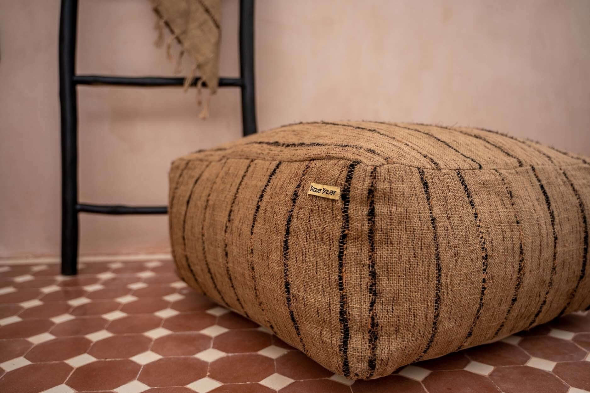 Katoenen poef in beige en zwart strepen op geometrische tegelvloer, stijlvolle en functionele woonaccessoire.