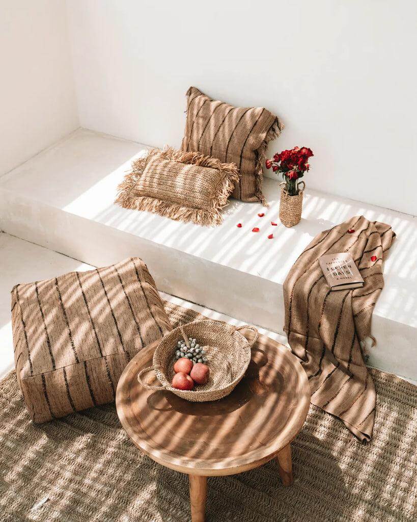 Stijlvolle beige en zwarte poef met kussens en decor op een zonnig terras.